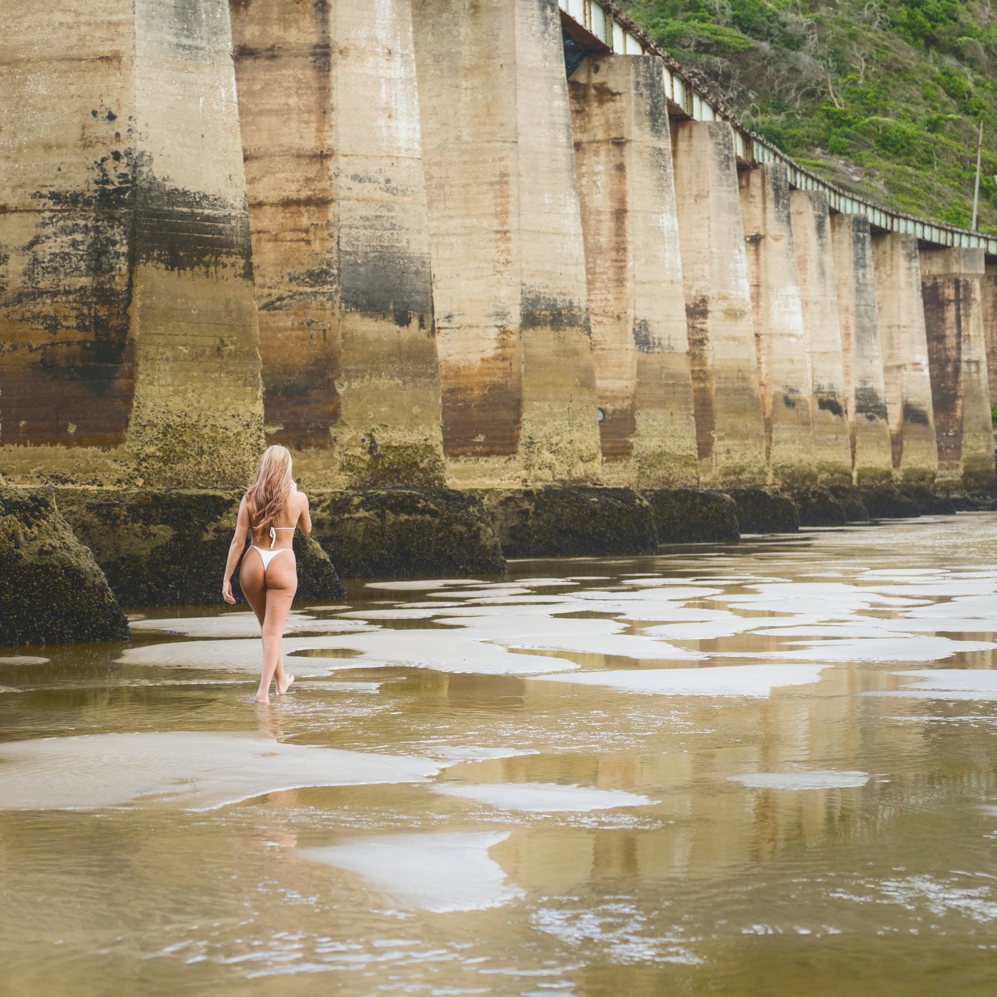 Swimsuit model in white bikini walking alongside the kaaimans river railway bridge